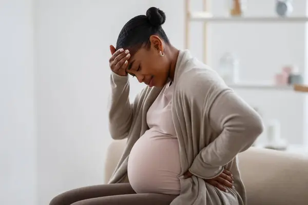 妊娠期偏头痛非洲裔美国人期待着家里头疼的女人 坐在舒适的客厅里的沙发上 摸着头 感觉不舒服 复制空间 — 图库照片