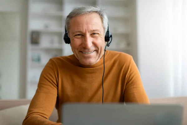 Closeup of old man using headset and laptop computer at home, working remotely, have online meeting with colleagues or client. Job opportunities for seniors concept, copy space