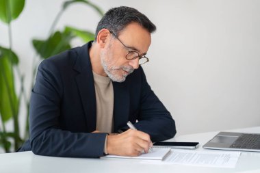 Takım elbiseli yaşlı Avrupalı işadamı, evrakları imzalarken, modern ofiste sözleşmeyle çalışıyor. İş dünyası, teknoloji ve çoklu görev ile başlangıç için fikir oluştur