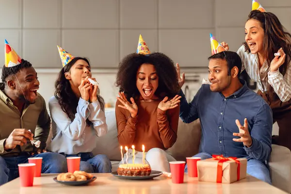 Diverse group of friends enjoying birthday party with cake and laughter, sharing moments of happiness celebrating together in modern living room at home. Bday celebration concept