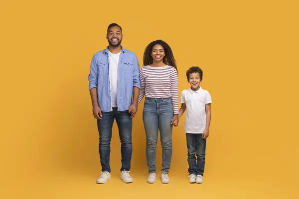 鮮やかな黄色の背景 幸せな若いアフリカ系アメリカ人の両親とスタジオの設定でポーズをとっている男性の子供と一緒に手を握っている19歳の息子と微笑む黒人の家族の肖像 — ストック写真