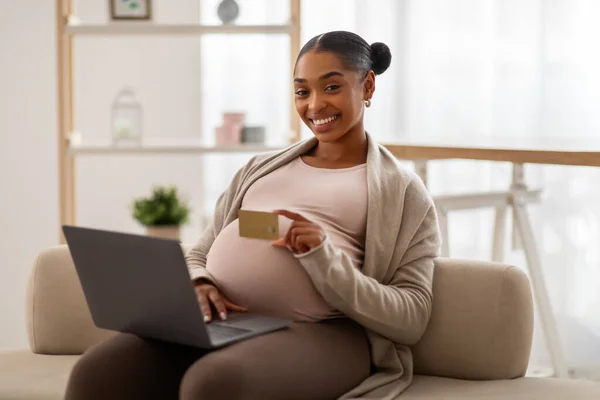快乐的年轻非洲裔美国孕妇使用电脑笔记本电脑和信用卡 享受在轻便客厅里生孩子的乐趣 网上购物 分娩准备 在家做母亲 — 图库照片