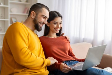 Hafta sonu eğlencesi. Mutlu genç çift evde dizüstü bilgisayar kullanıyor, Milenyum eşleri oturma odasında dinleniyor, film izliyor ya da internetten alışveriş yapıyor, uzay kopyalıyor.