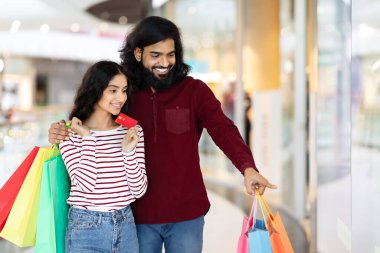 Kolay ödeme. Neşeli genç Hintli çift alışveriş merkezinde birlikte alışveriş yapıyor. Hintli adam elinde kredi kartıyla kız arkadaşına sarılıyor, vitrinlere bakıyor, boşlukları kopyalıyor.