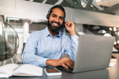 İşçi Merkezi 'ni ara. Kulaklık takan Hintli genç bir adamın portresi, yakışıklı bir Doğulu müşteri hizmetleri operatörü kameraya bakıyor ve gülümsüyor,