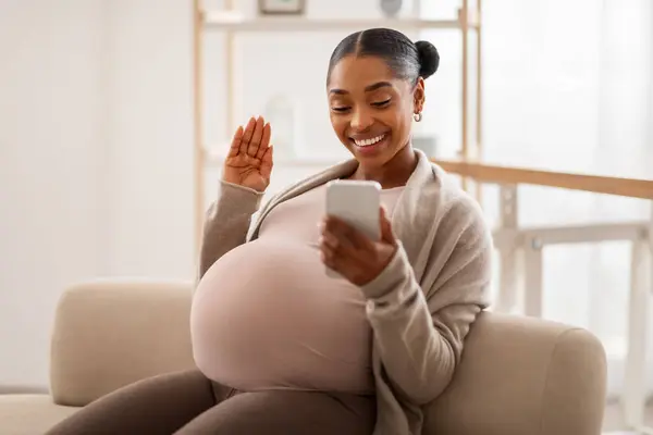 积极的年轻黑人孕妇 肚子大 坐在舒适客厅的沙发上 与丈夫或朋友通电话 在小屏幕前挥挥手微笑 复制空间 — 图库照片