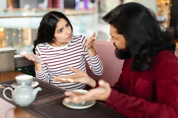 Relationship problems, divorce, separation concept. Unhappy young indian woman having conflict with her boyfriend at cafe. Millennial couple fighting, having difficulties or misunderstanding