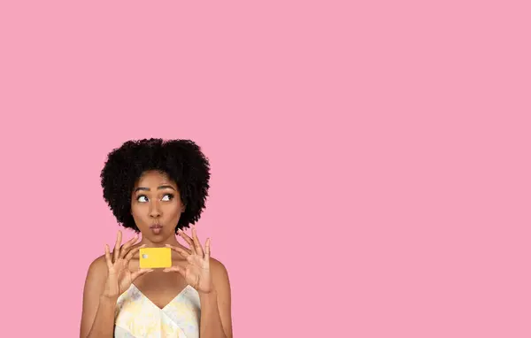 千年前的非洲裔美国妇女 卷曲的头发 带着一张信用卡嬉闹地把她的嘴唇 在粉红的背景下做着一张沉思的脸 带着复制的空间 工作室 — 图库照片