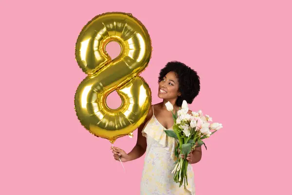 ジョイフルな若いアフリカ系アメリカ人女性は 彼女の8周年を祝います 黄金の番号8バルーンとピンクの背景に対する新鮮なチューリップの束 スタジオ — ストック写真