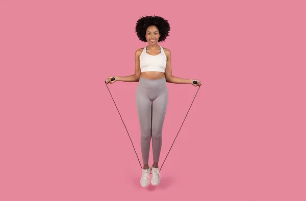 快乐的黑人女人 准备开始跳绳跳绳 身穿白色运动胸罩和灰色腿 衬托着充满活力的粉色背景 — 图库照片