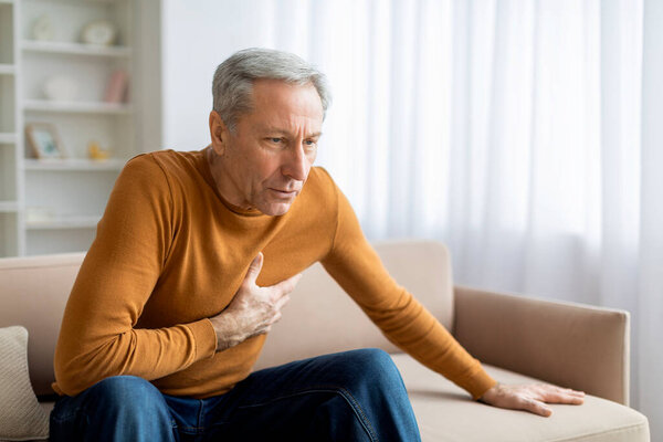 Старший страдает от сердечного приступа дома. Мужчина сжимает грудь. Боль, возможный сердечный приступ. У дедушки сердечный приступ дома. Человек с болью в груди, пустое пространство