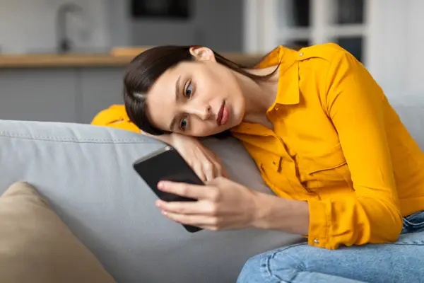Zaniepokojona Młoda Kobieta Pochylona Kanapie Uważnie Wpatrująca Się Ekran Smartfona — Zdjęcie stockowe