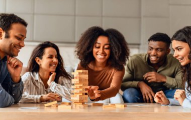 Neşeli uluslararası öğrenciler mutfak masasının etrafında toplanıp neşeli masa oyunları oynuyorlar, birlikte ahşap kule inşa ediyorlar, hafta sonları boş zaman geçiriyorlar, ev partileri yapıyorlar.