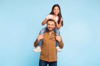 En iyi baba. Gururlu beyaz bir baba, küçük kızını omuzlarında taşırken, Mavi Stüdyo 'ya karşı birlikte poz verirken, kameraya gülümserken,