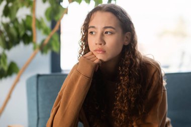 Genç bir kız evdeki koltukta oturup ilgisizlik ve zihinsel sağlık sorunlarını gençlik çağında tasvir ederek kendini üzgün hissediyor. Yalnız ve hayal kırıklığına uğramış genç bir kadının portresi.