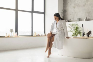 Depodan sonra kusursuz bacaklara dokunan, evdeki banyoda otururken poz veren, tam uzunlukta, kopyalama uzayı. Kılları ve Vücut Bakımı