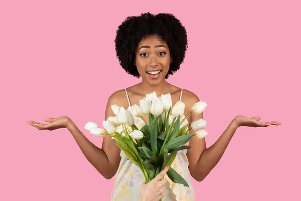 令人惊讶和快乐的非裔美国千禧年女性展示了一束郁郁葱葱的白色郁金香 带着嬉笑的表情 与充满活力的粉色背景 工作室 人的情感 — 图库照片
