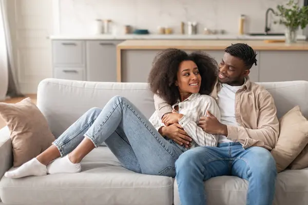 幸せな若い結婚した黒人のカップルは居間でカジュアルな週末を楽しんで ソファーで座って 居心地の良い家のインテリアで一緒に抱擁しながら愛を楽しんでいます — ストック写真