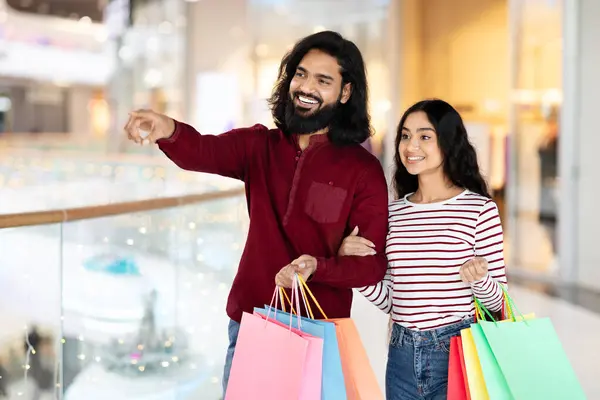 一緒にモールでショッピングをする幸せなインドのカップル 季節のセールスと割引を楽しむ 百貨店で買い物バッグで歩いている間にショーケースを見ている陽気な東部の配偶者 — ストック写真
