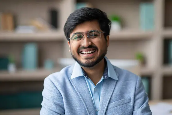 Successful Businessman. Portrait of happy young Indian entrepreneur man wearing blue blazer, smiling friendly at camera, standing with confidence in office, reflecting welcoming corporate culture