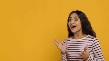 Yazı ya da reklam için boş fotokopi alanına bakan, sarı stüdyo arka planında izole edilmiş poz veren güzel Hintli genç bayan hayrete düştü.
