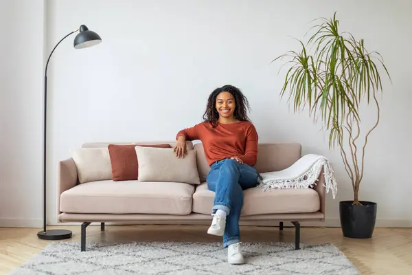 Joven Alegre Mujer Negra Sentada Cómodamente Sofá Moderno Con Cojines — Foto de Stock