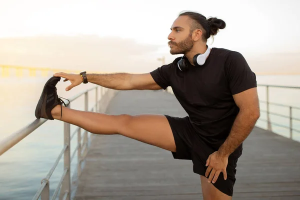 适合欧洲小伙子穿运动服在外面练习站立腿伸展 促进健康的生活方式 锻炼肌肉柔韧的动力 海边的运动与健康 — 图库照片
