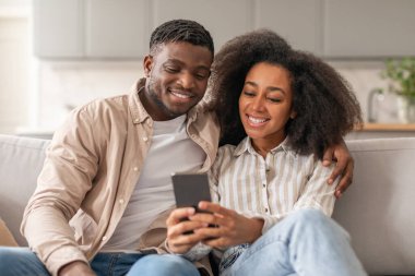 Siyahi milenyum eşleri cep telefonlarını mesaj atmak ve web sörfü yapmak için kullanırken, evdeki kanepede otururken kucaklaşırken, modern iletişim kavramını sergiliyorlar.