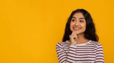 Harika bir teklif, heyecan verici bir anlaşma. Gülümseyen, çekici, uzun saçlı, Hintli bir kadın. Boş fotokopi alanı modeline bakıyor. Sarı stüdyo arka planında izole edilmiş, çenesine dokunuyor.