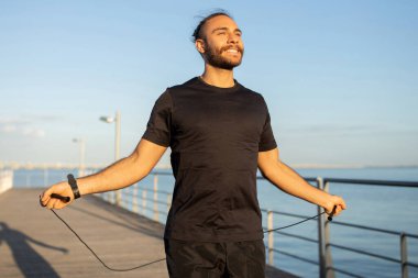 Yaz Kardiyo Çalışması. Aktif sporcu, deniz kenarındaki bir rıhtımda ip atlıyor dışarıda çalışıyor, fitness motivasyonunu ve sağlıklı spor yaşam tarzını destekliyor, gülümsüyor.