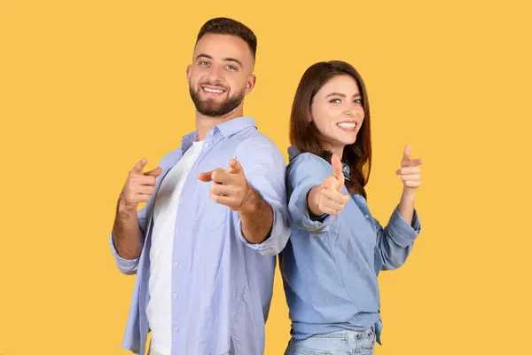 穿着斜纹棉布的快乐的男女青年自信而灿烂地指着相机 站在黄色的背景上 代表着积极和积极的一面 — 图库照片