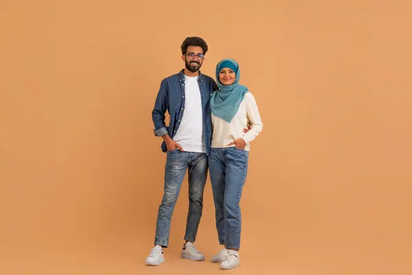 ベージュのスタジオの背景に立っている幸せな現代ムスリムのカップルの肖像画 笑顔のアラビアの配偶者男性とヒジャブが抱擁し カメラを見ている女性 コピースペースとの完全な長さ — ストック写真