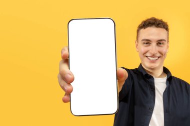 Harika bir online teklif. Neşeli, yakışıklı genç adam beyaz ekranlı akıllı telefonu gösteriyor. Tasarruf kremi, reklam için kopya alanı, sarı arka plan.