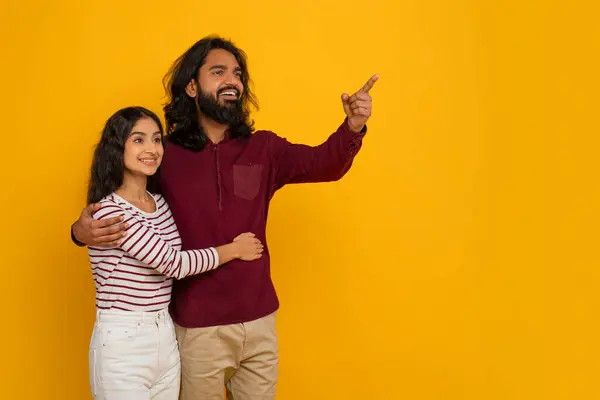 笑顔ミレニアムインドのカップル男性と女性は 広告のための空白のコピースペースを抱擁し 指差し 素晴らしいオファーを示し 2つの黄色のスタジオの背景のための取引 — ストック写真