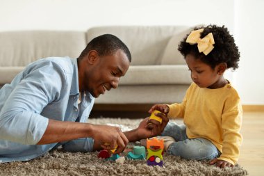 Aile zamanı konsepti. Şirin kıvırcık çocuk, Afrikalı Amerikalı kız babasıyla oynuyor, mutlu siyah bebek ve babası renkli blokları olan bir kule inşa ediyorlar, ev içi, yakın çekim.
