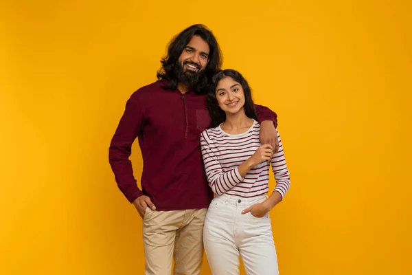 人間関係 黄色いスタジオの背景に抱擁する若いインドのカップルを愛する ハッピーミレニアル東部の男性と女性は カメラで抱擁し 笑顔で結びついています — ストック写真