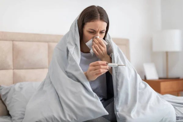 Young Woman Wrapped Blanket Sits Bed Blowing Her Nose Worriedly — Stock Photo, Image