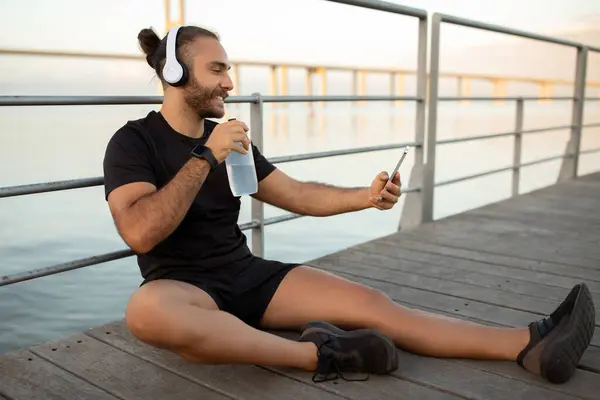 Sporty Man Activewear Using Cellphone Earphones Holding Water Bottle While — Stock Photo, Image