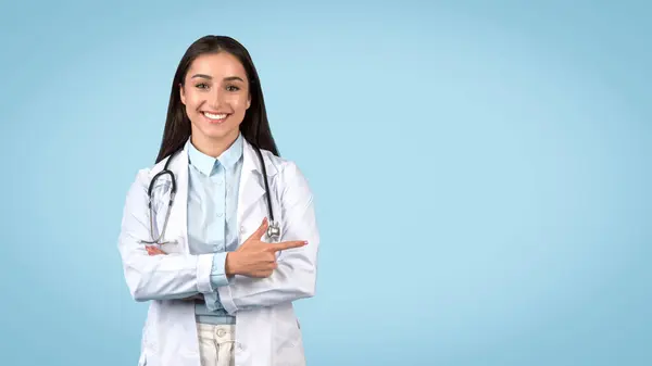 広々としたブルーの背景 パノラマ ホワイトラボコート スタティスコープで 魅力的な笑顔で自由な空間を指摘する放射性女性の医師 — ストック写真