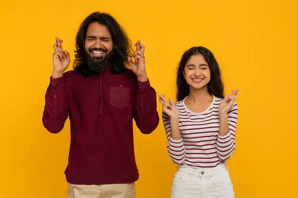迷信的な若いインド人男性と女性は 目を閉じて 黄色いスタジオの背景に指を交差させました エキサイティングなミレニアルヒンドゥー教のカップルジェスチャー 願いを作る — ストック写真