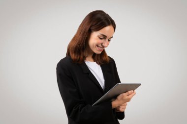 Parlak siyah takım elbiseli, nişanlı ve beyaz bir iş kadını dijital tablete odaklanırken gülümsüyor. Modern profesyonelliği ve bağlantılılığı, stüdyoyu işaret ediyor. İş, iş.