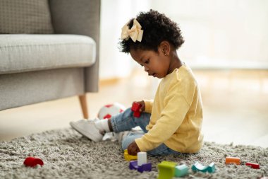 Sevimli, mutlu, Afro-Amerikan bebek bebek evde çocuklarla oynarken oturma odasında halı döşemesinde oturuyor. Renkli oyuncaklar kullanarak gülümseyen sevimli çocuğun portresi, kopyalama alanı