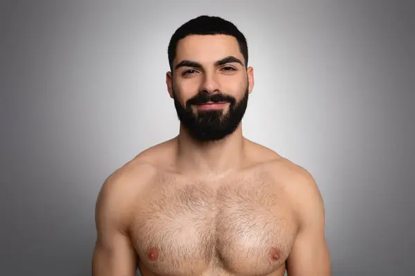 演播室拍摄的英俊的黑发大胡子阿拉伯男子穿着灰色背景的衬衫 对着相机微笑 淋浴后展示出优美的运动体态 — 图库照片