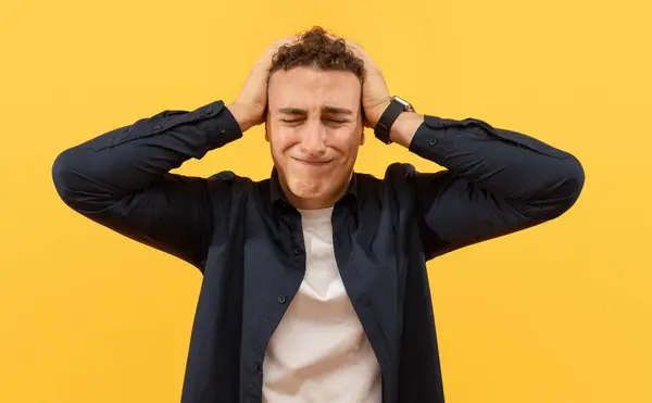 Stressed young caucasian man wears casual basic clothing touchign his head with closed eyes isolated on plain yellow background, feeling exhausted, studio portrait