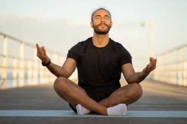 Farkındalık. Fitness 'teki Sakin Genç Adam Lotus pozisyonunda oturmuş, dışarıda Om jesti yapıyor, Yoga egzersizi sırasında dinleniyor ve deniz iskelesinde meditasyon yapıyor, gözleri kapalı.