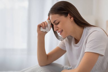 Telaşlı genç bir kadın yatakta oturuyor, ağlıyor ve gözyaşlarını beyaz bir mendille siliyor. Parlak yatak odasında üzüntü ya da duygusal sıkıntı anı yaşıyor.