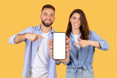 Gündelik gözaltında gülümseyen genç bir çift ve boş akıllı telefon ekranına işaret ederek, güneşli sarı arka planda bir uygulama veya web sitesi öneriyor,