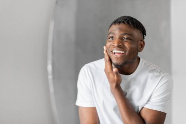 Yakışıklı siyahi adam banyoda dikilip aynadaki yansımasına bakıyor ve yüzüne dokunuyor. Şımartıldıktan ve kendine baktıktan sonra görünüşünden memnun. Günlük bakım rutini ve cilt bakımı