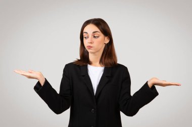 Kuşkulu bin yıllık Kafkasyalı iş kadını avuçlarını dengeleyici bir jest olarak kaldırmış siyah takım elbiseli, seçenekleri tartarmış gibi şüpheli bir yüz ifadesi takınıyor ya da bir seçimi sorguluyor.