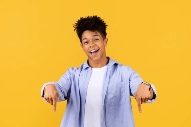 Neşeli siyah adam iki eliyle aşağıya doğru işaret ediyor, izleyicileri aşağıdaki ilginç bir şeye bakmaya davet ediyor, güneşli sarı arka plana karşı.